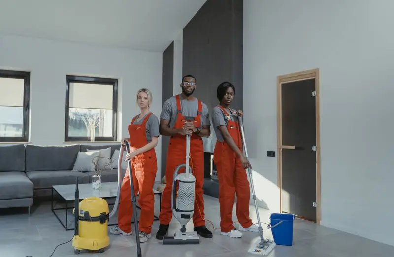 Drie schoonmakers met stofzuigers in een woonkamer