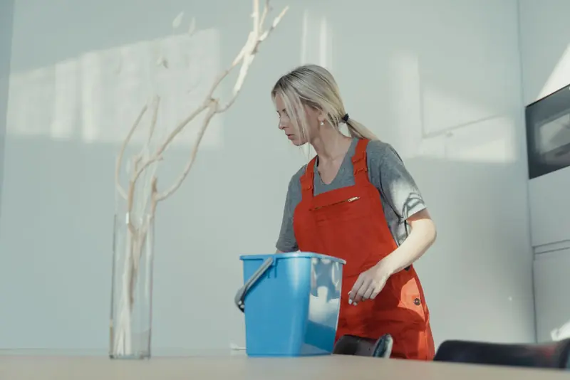Schoonmaakster met emmer maakt een kantoorruimte schoon